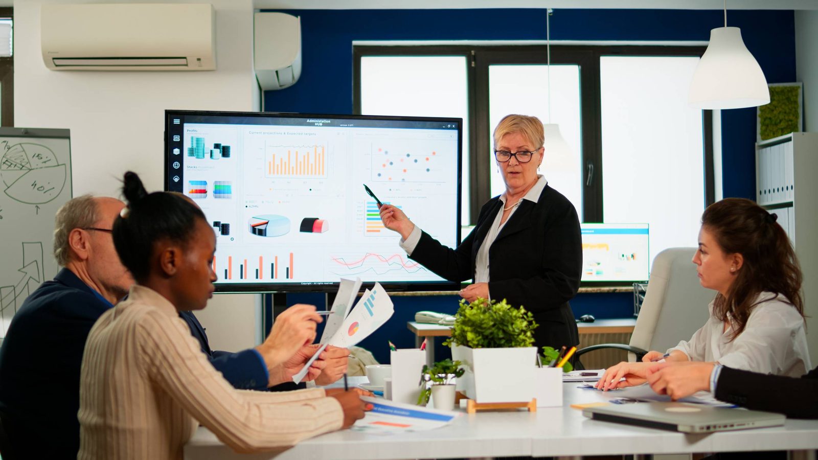 Manager presenting analytics charts on a digital screen to a team in a meeting room