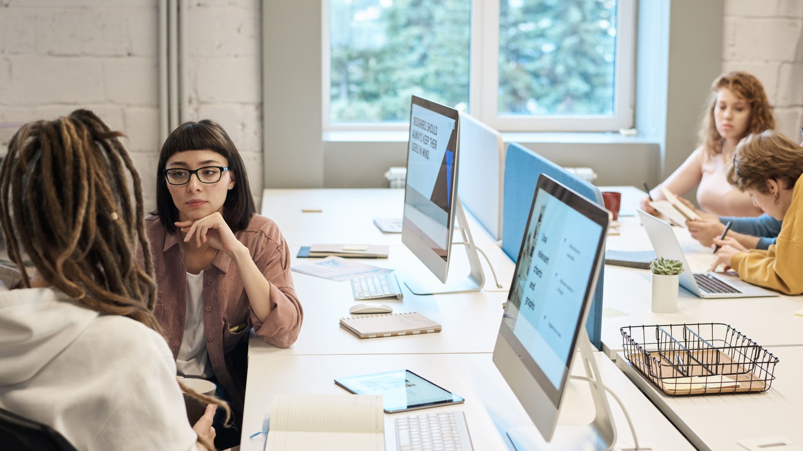 Colleagues talking at a shared desk with monitors in a bright open office