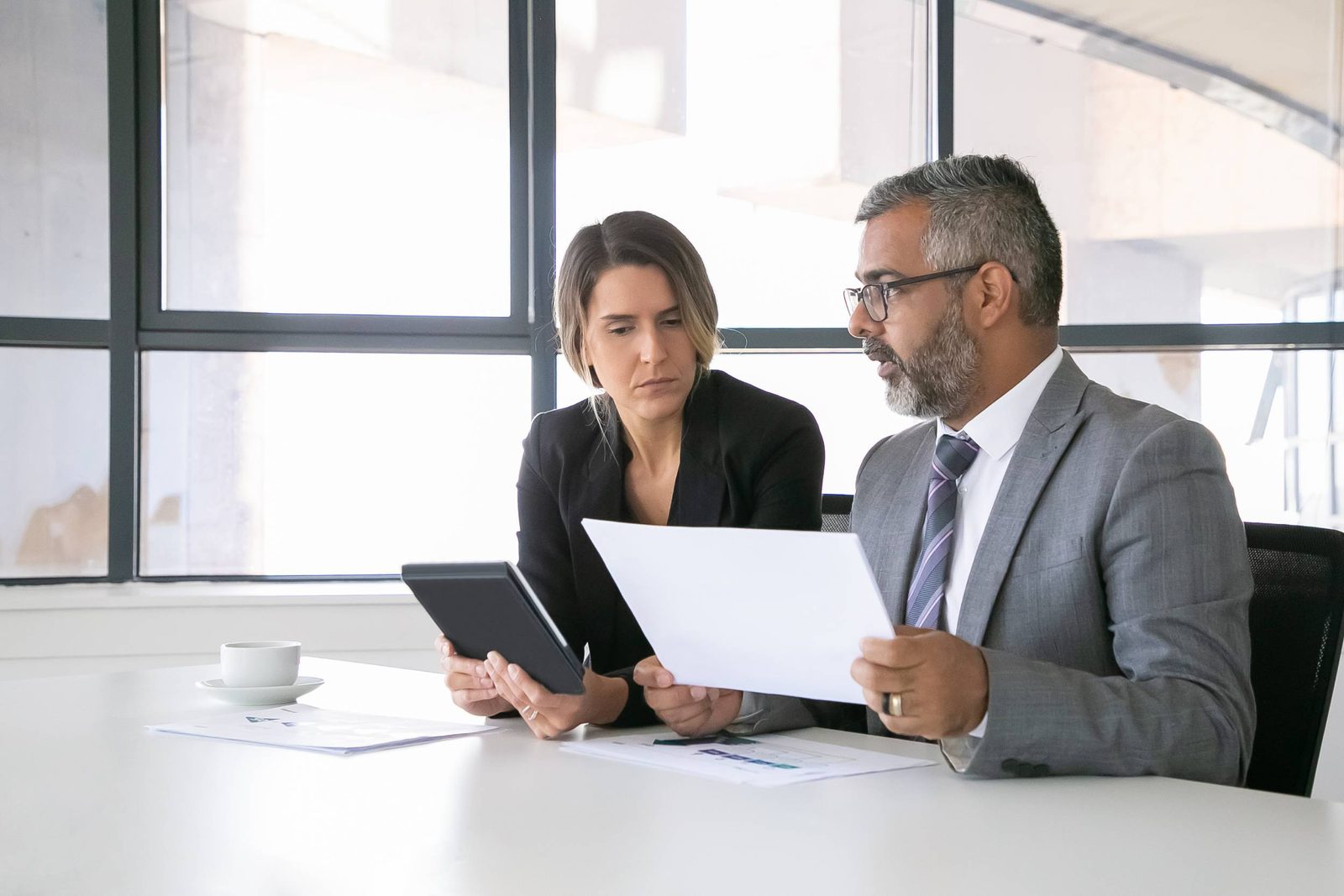 Two colleagues reviewing time and payroll records with a tablet and printed report