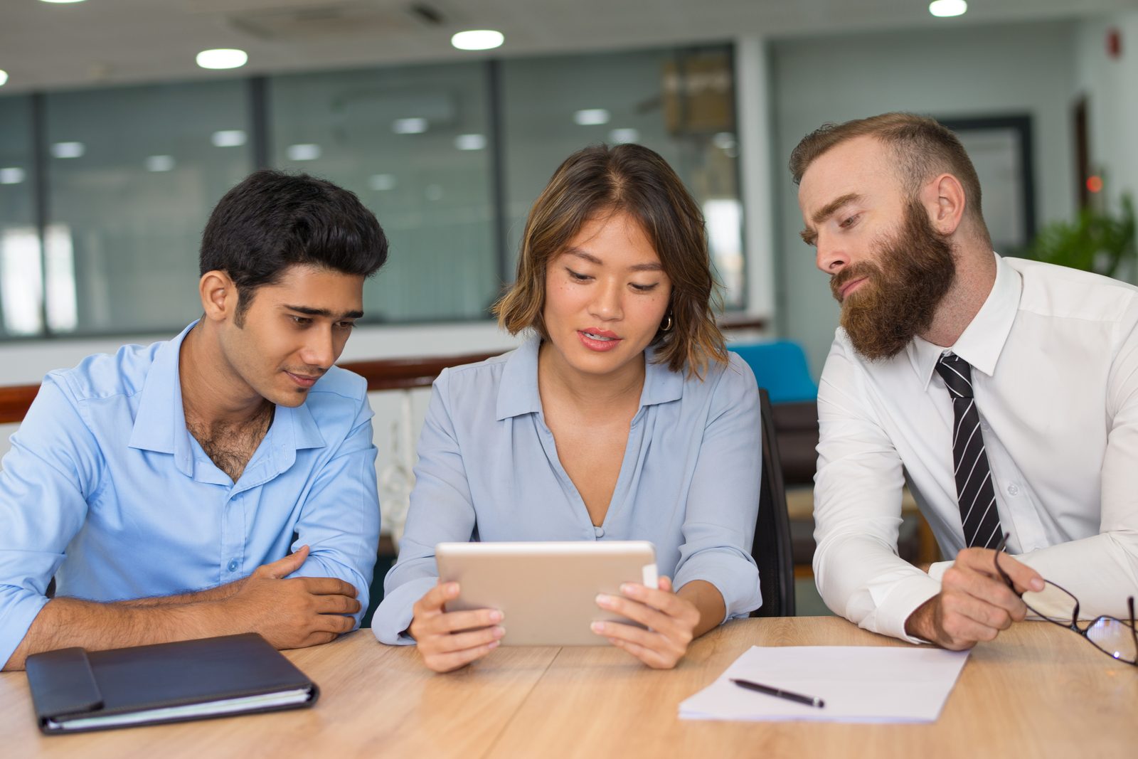 Three colleagues reviewing team productivity data on a tablet at a meeting table